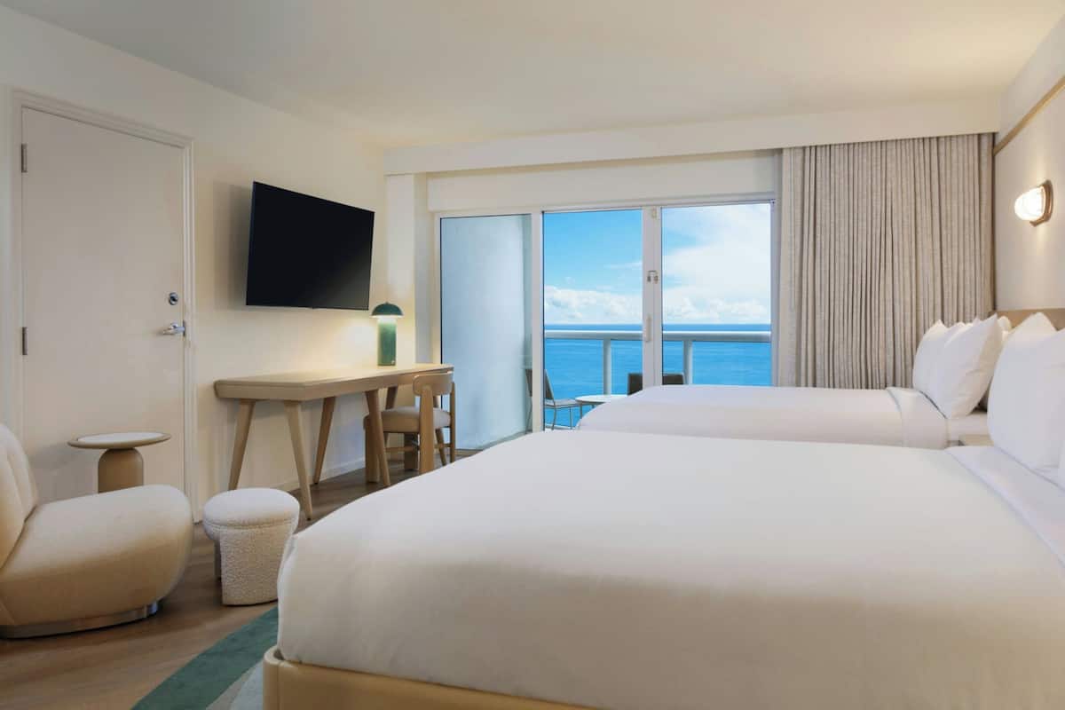 Une chambre d’hôtel avec deux lits, un bureau, une chaise, une télévision et une vue sur la mer.