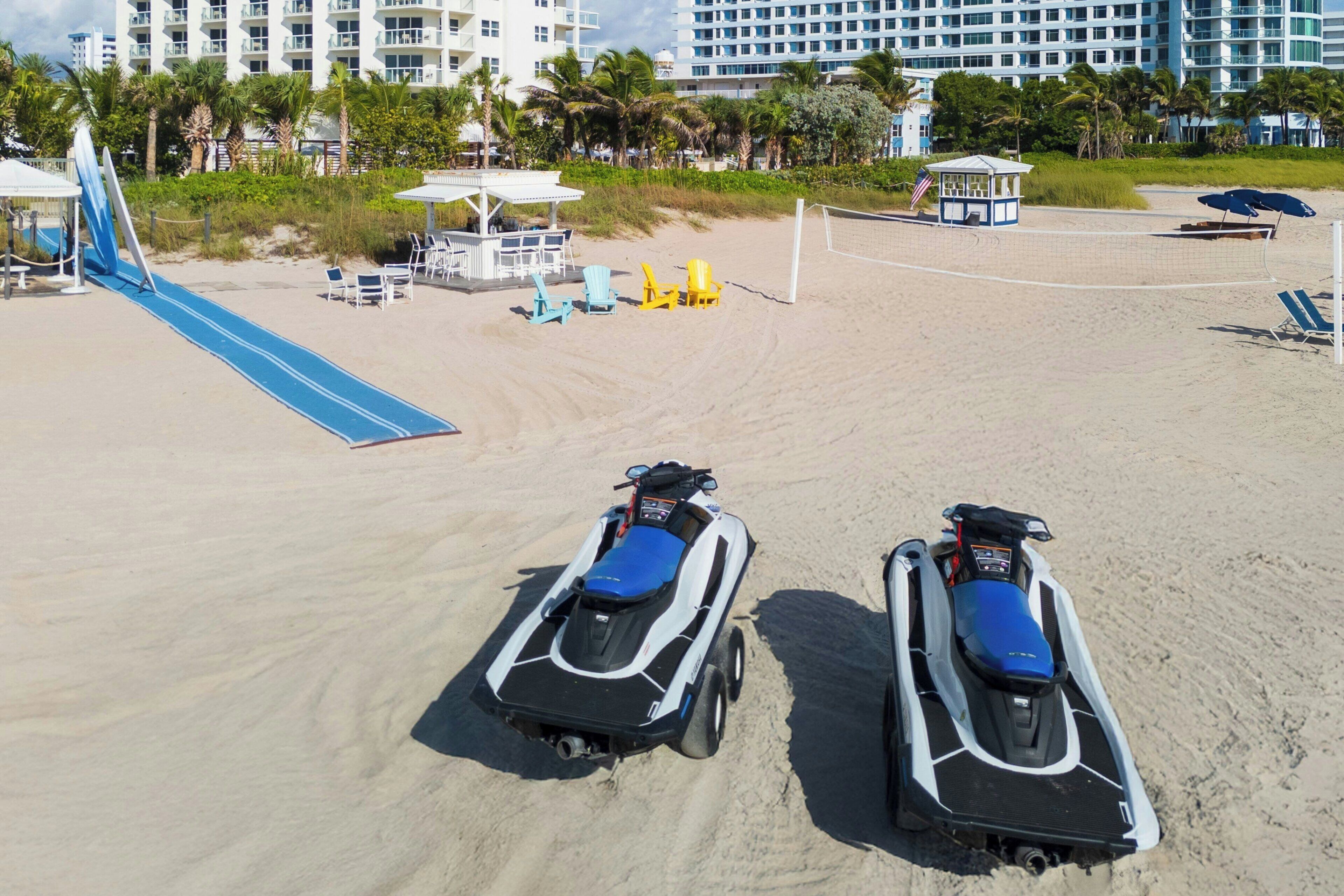 A beach with two jet skis, a volleyball net, and a lifeguard tower.