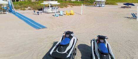 A beach with two jet skis, a volleyball net, and a lifeguard tower.
