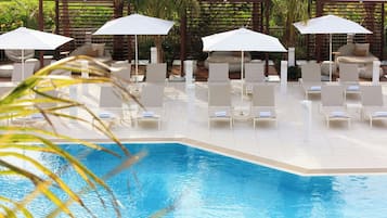 A poolside area with lounge chairs and umbrellas, surrounded by a wooden pergola and palm trees.