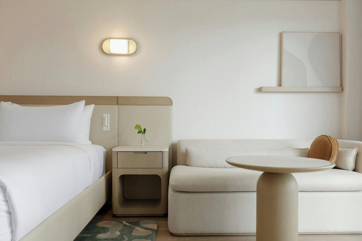 Une chambre d’hôtel comprenant un lit, une table de chevet avec une plante, un canapé, une petite table ronde et un luminaire fixé au mur.