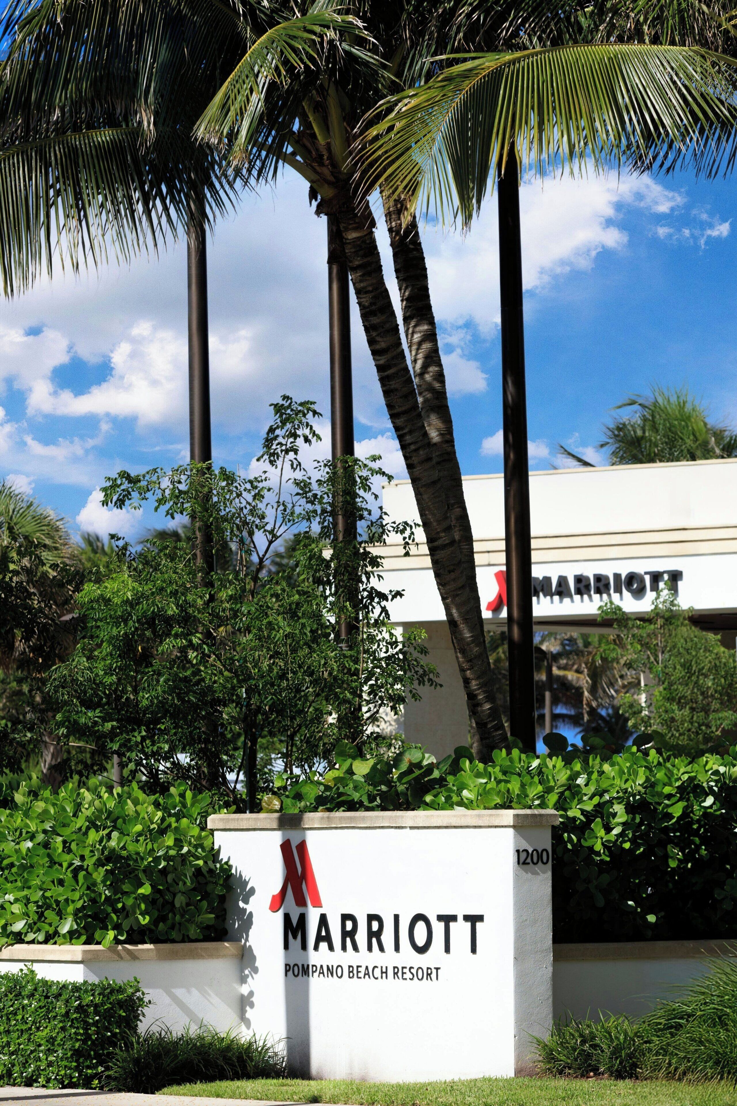 A Marriott hotel sign with palm trees and greenery.