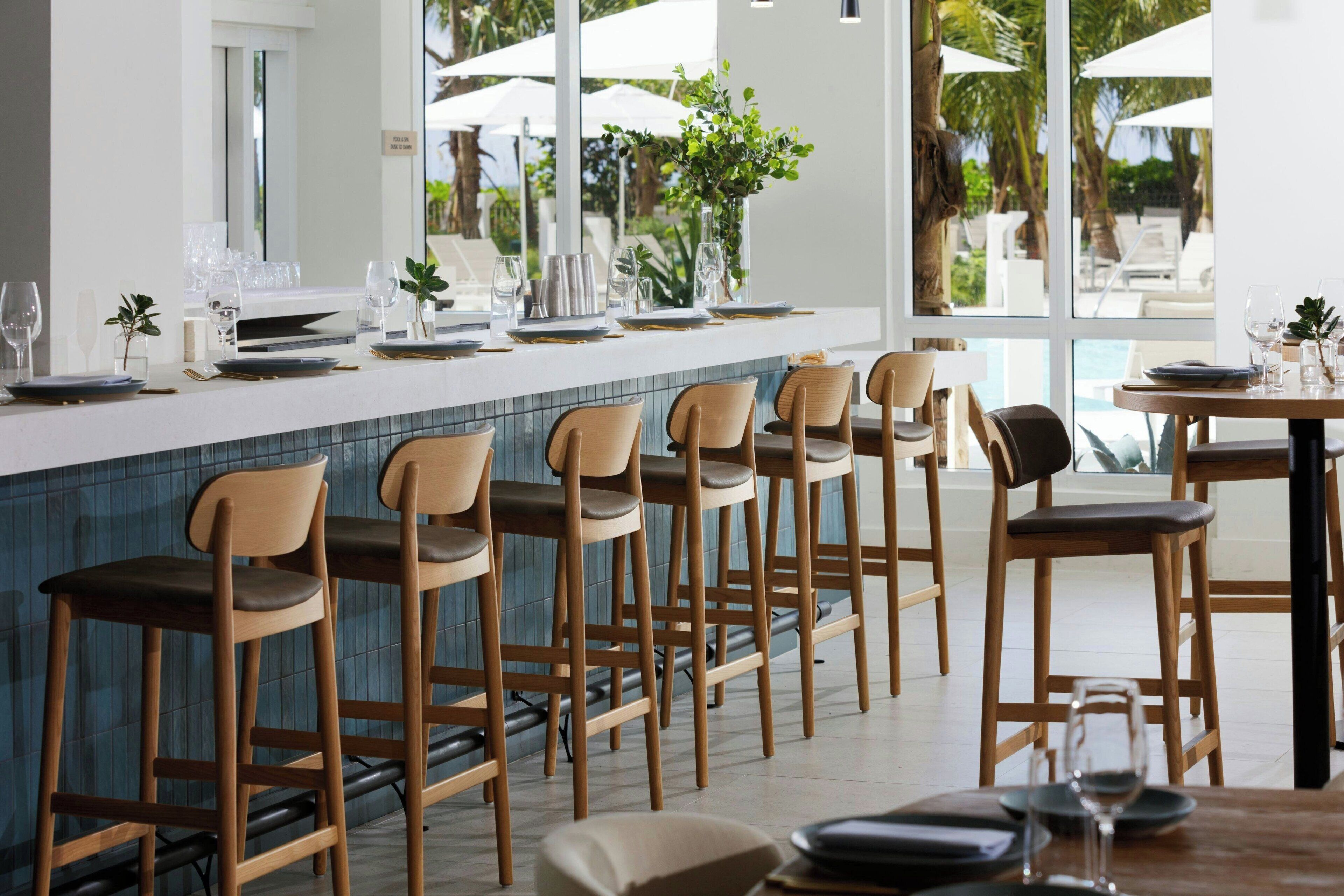 Un espace bar avec des tabourets hauts et un comptoir, une vue sur la piscine et un cadre extérieur de style tropical.