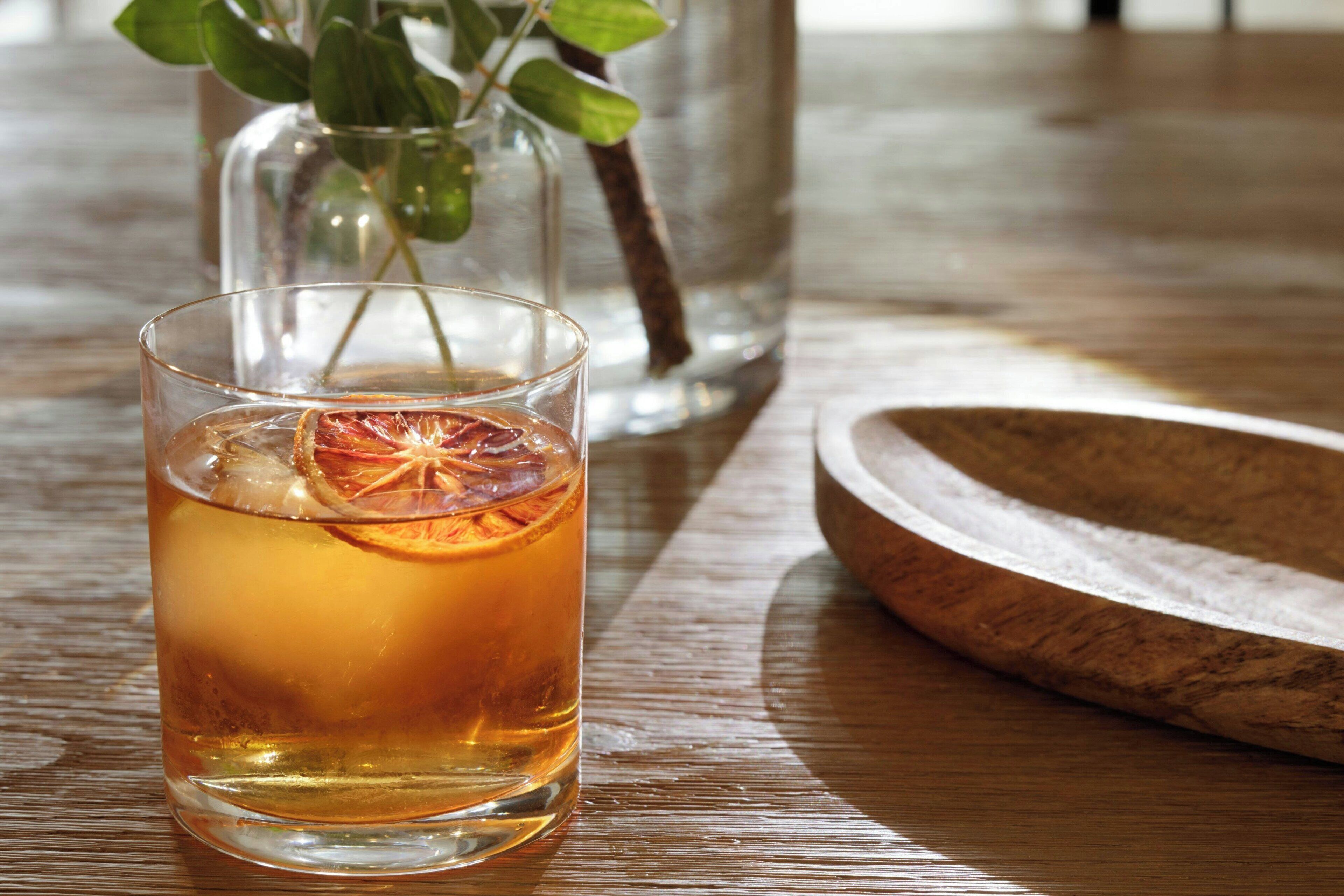 A glass of amber-colored beverage with a dried orange slice on a wooden table.