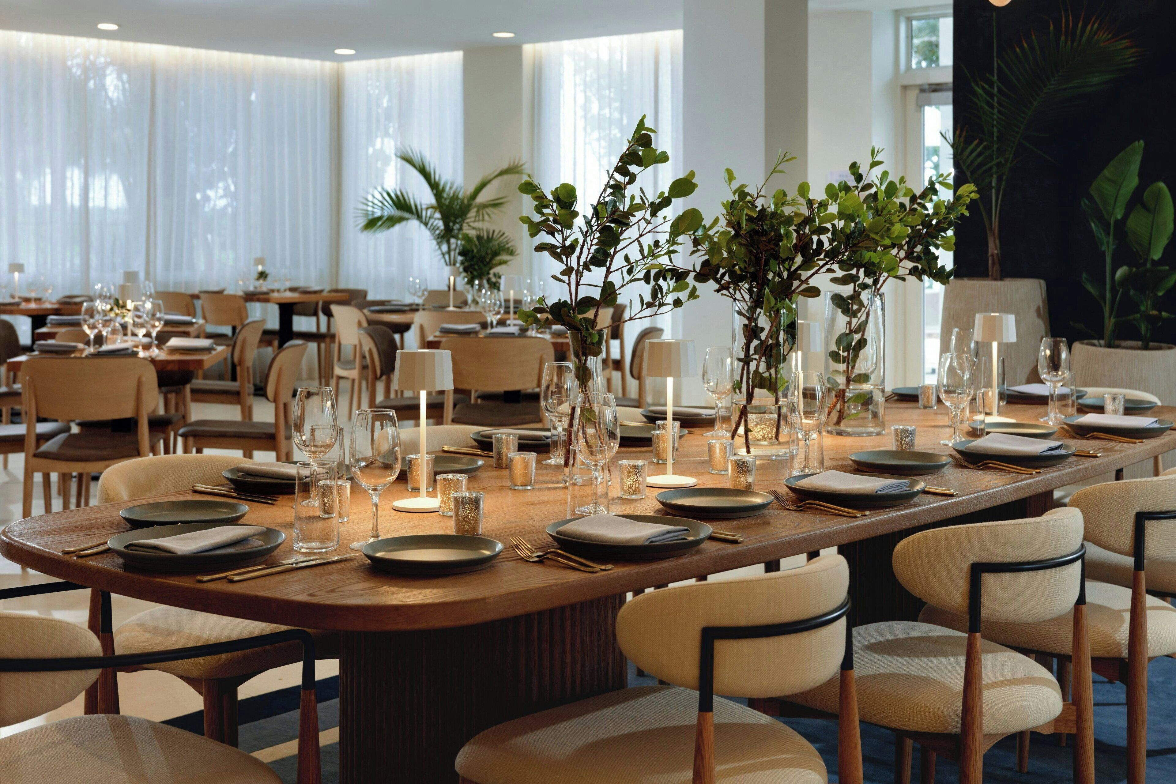 A dining area with round tables set for service, featuring glassware, plates, and candles.