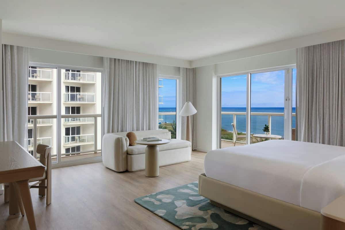 Une chambre d’hôtel dotée d’un grand lit, d’un canapé, d’une table à manger, d’une petite table et d’un balcon avec vue sur la mer.