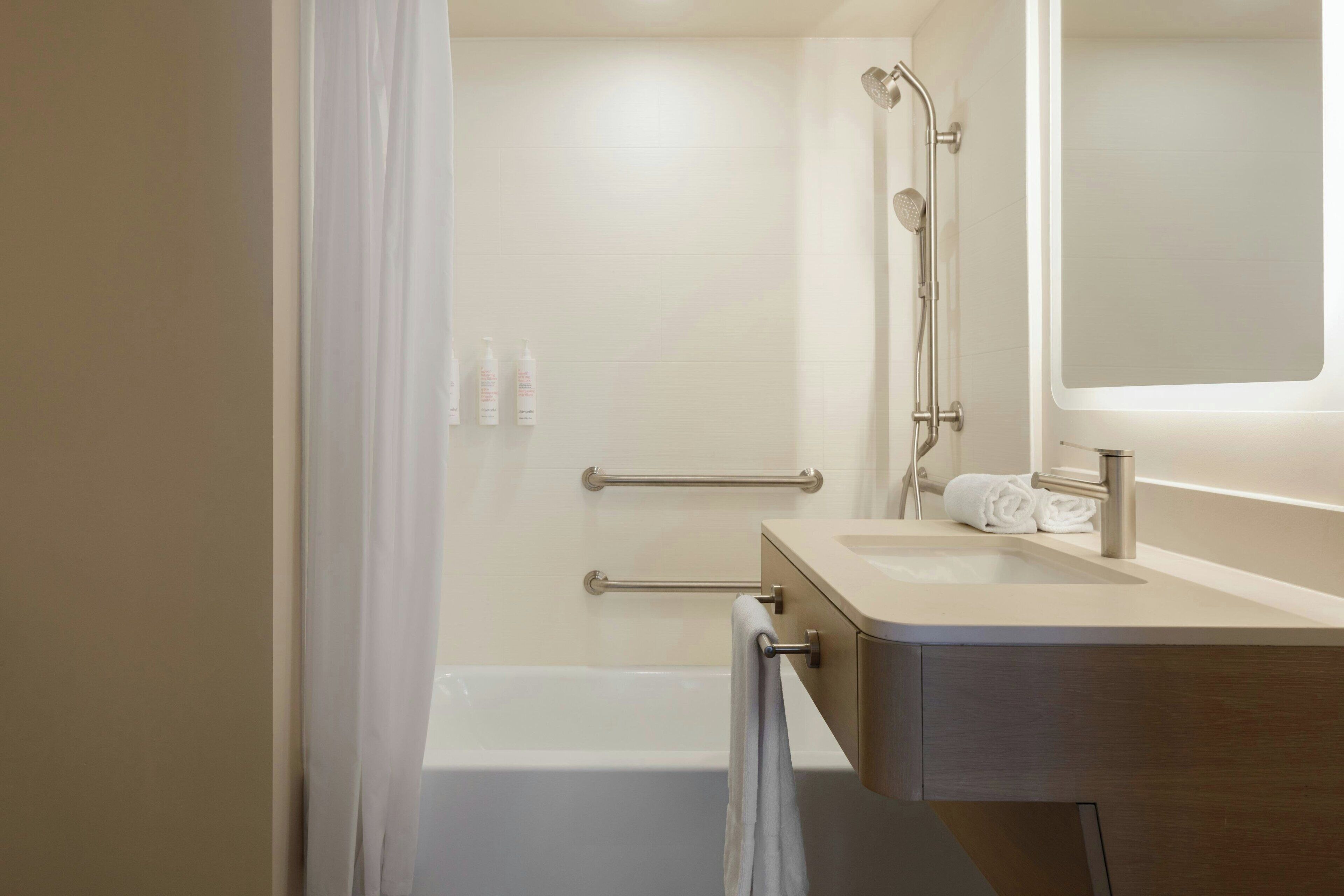 A modern bathroom with a bathtub, a shower with a handheld showerhead, a vanity with a mirror, and a towel rack.