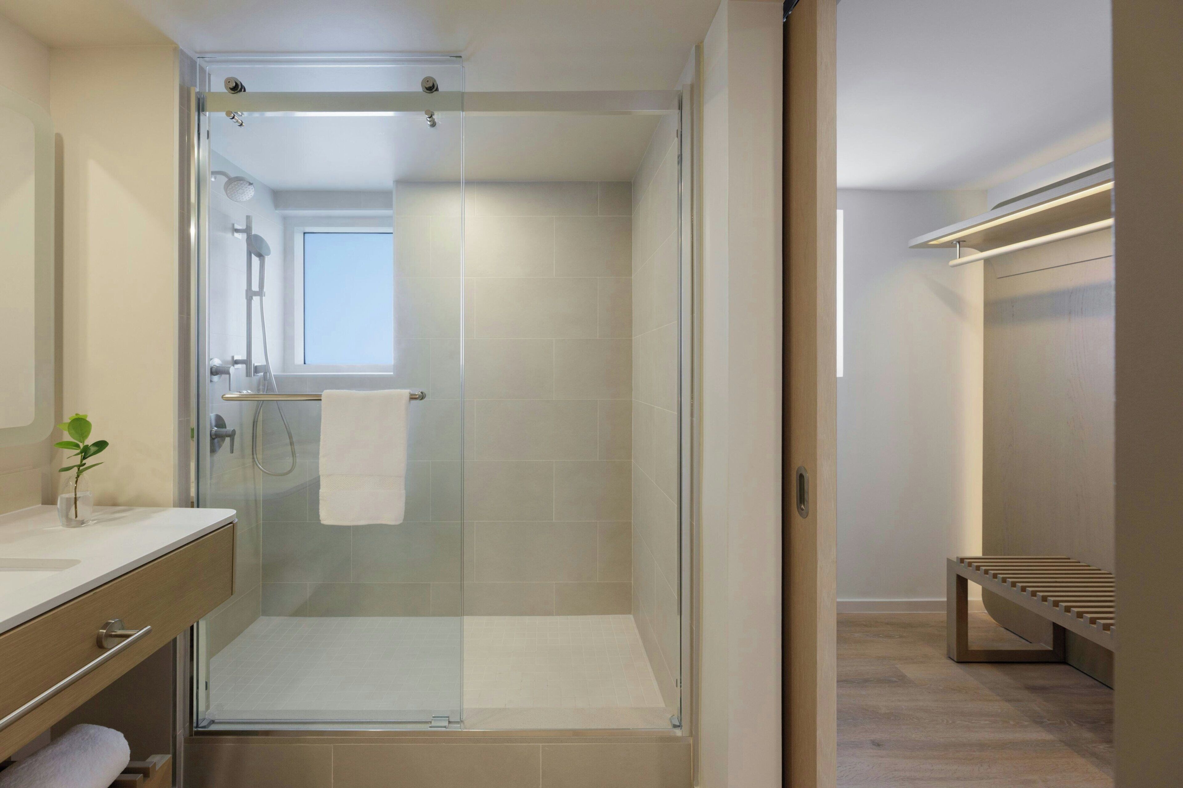 A modern bathroom with a glass-enclosed shower, a wooden bench, and a visible towel rack.