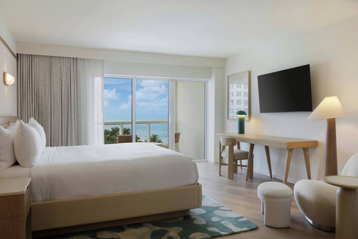 Une chambre d’hôtel avec un grand lit, un bureau, une chaise, une télévision et une vue sur l’océan.