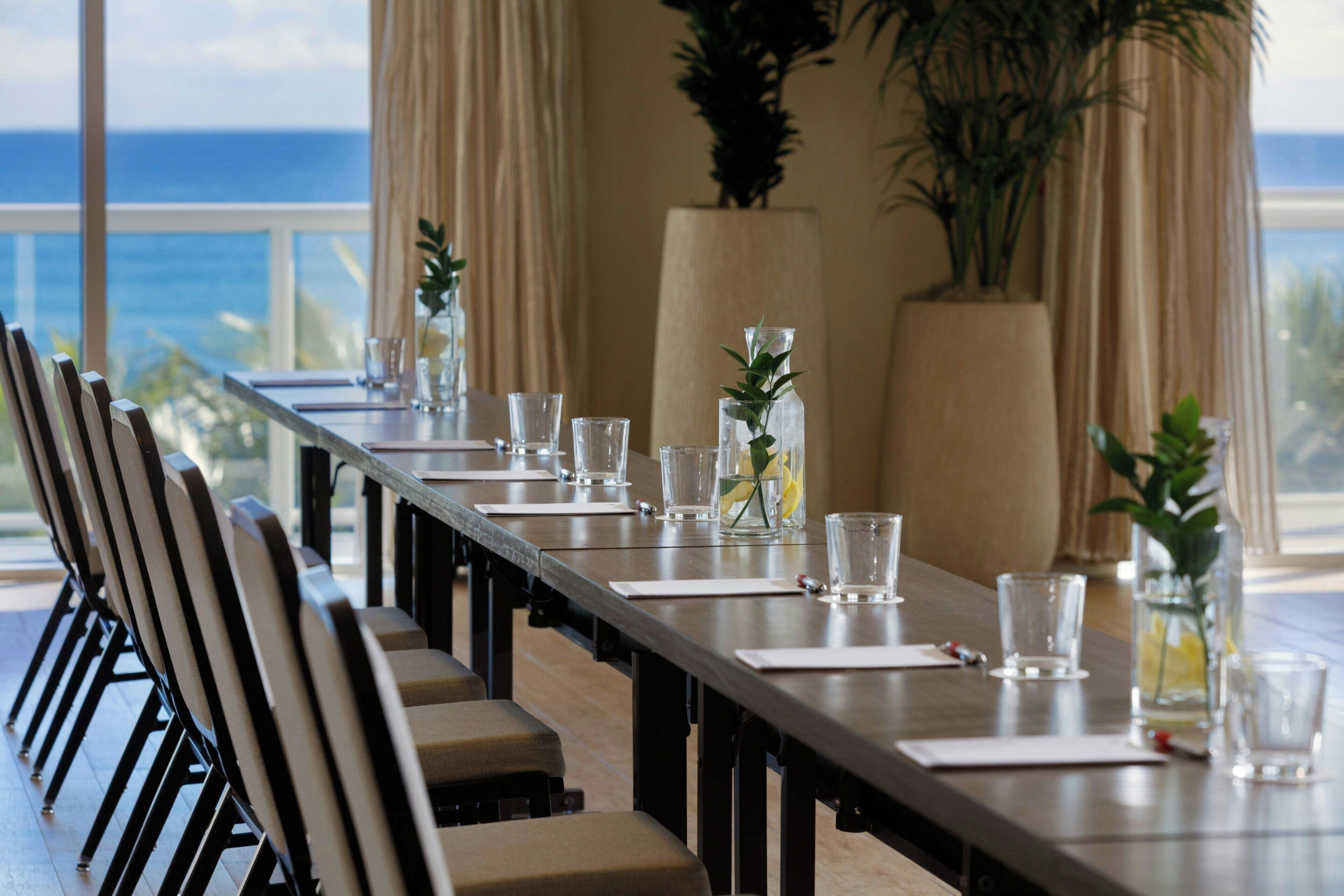 Une table de conférence préparée pour une réunion, avec des chaises, de la verrerie et des plantes en pot.