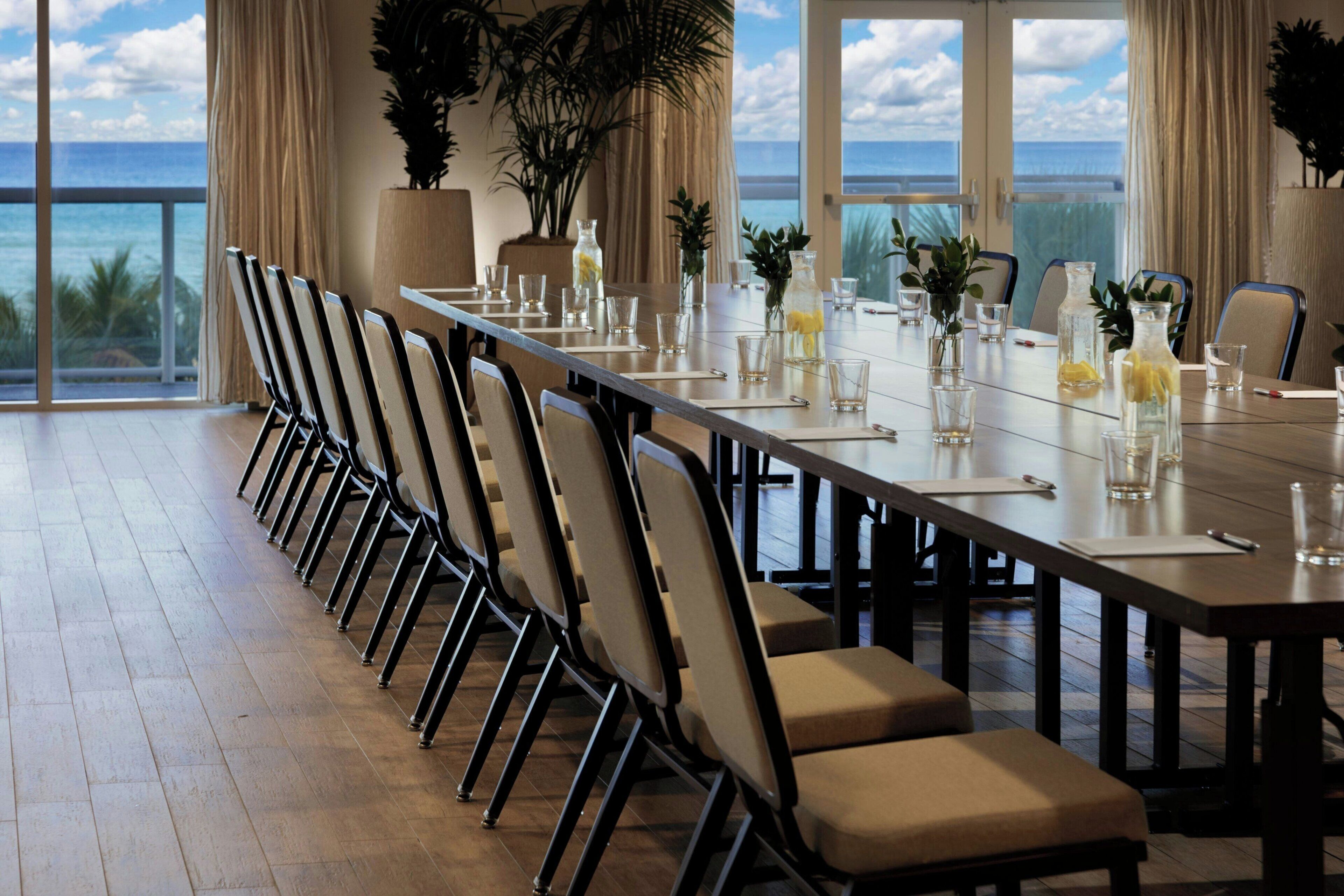 A long dining table with chairs, glassware, and potted plants.