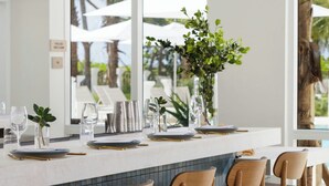 A bar area with a white countertop, multiple stools, and hanging pendant lights. - Fort Lauderdale Marriott Pompano Beach Resort (Pompano Beach)