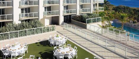 A rooftop dining area with round tables, white chairs, and a view of the ocean.