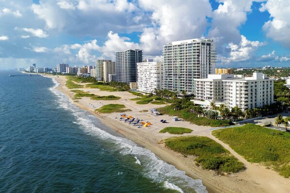 A coastal cityscape with high-rise buildings, a beach with umbrellas, and a clear sky.