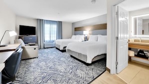 Habitación de hotel con cama, escritorio con silla, televisión y baño visible a través de una puerta abierta.