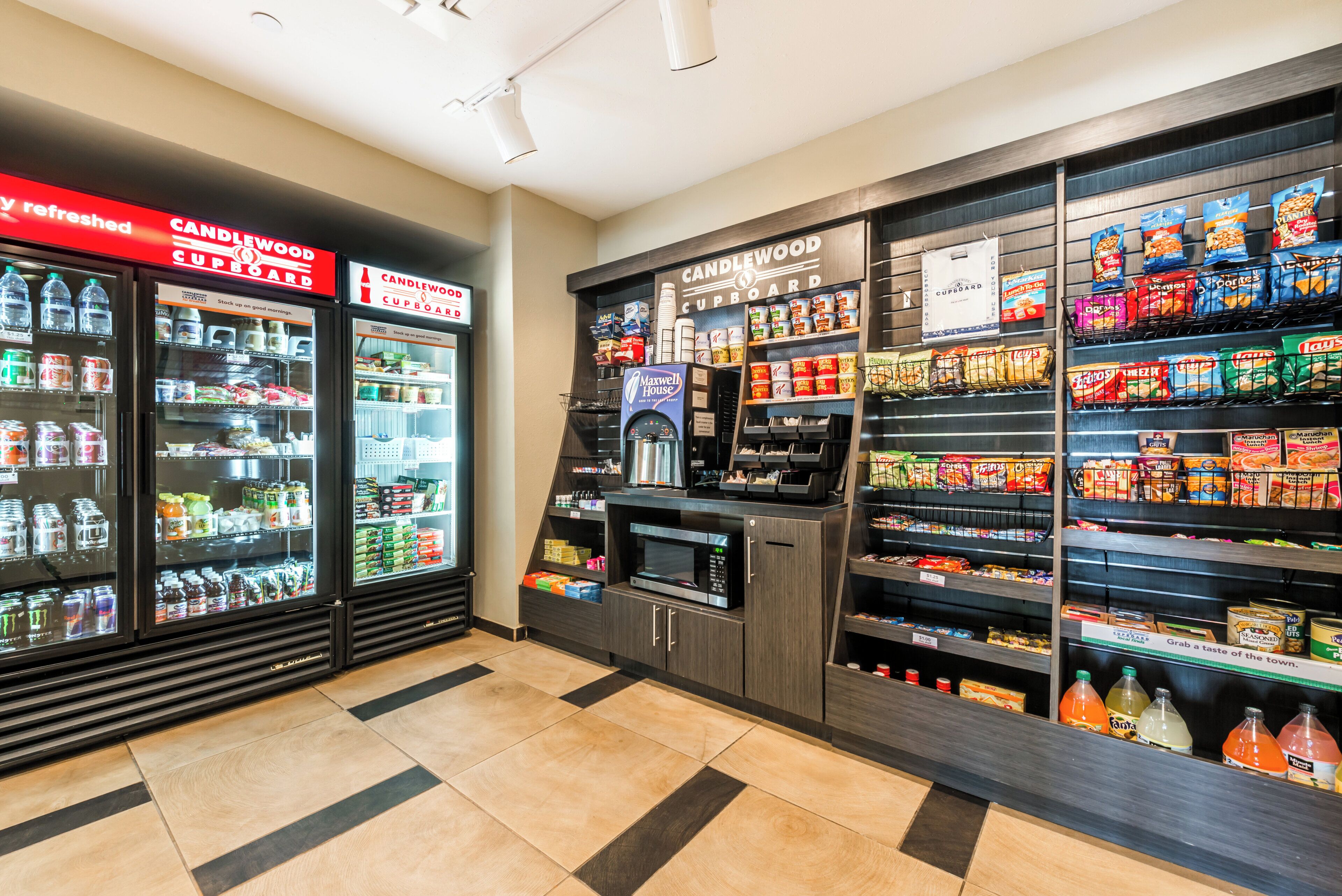 Una tienda de comestibles con dispensadores refrigerados para bebidas, una máquina de café y estantes llenos de aperitivos y bebidas.