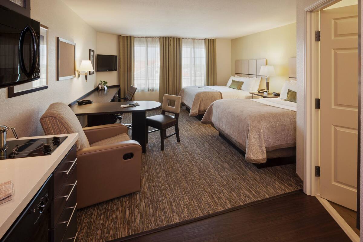 Une chambre d’hôtel avec une kitchenette, deux lits, une table à manger et un téléviseur.