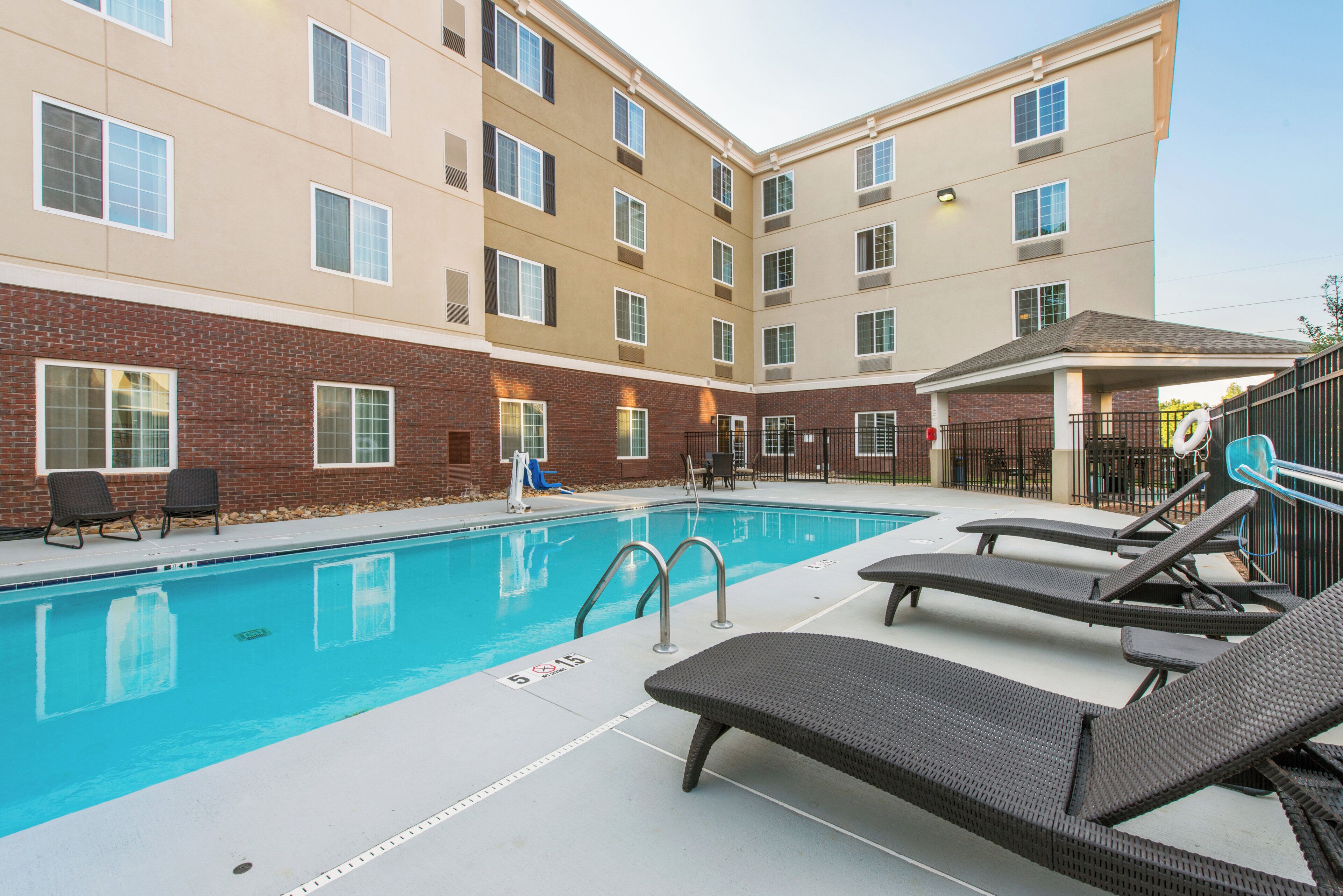 A swimming pool with lounge chairs and a brick building in the background.