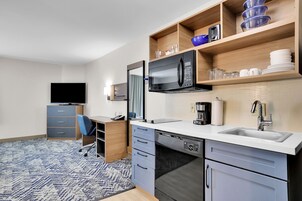 Una cocina moderna con microondas, cafetera y lavamanos. En la habitación contigua hay un televisor y un escritorio con silla.