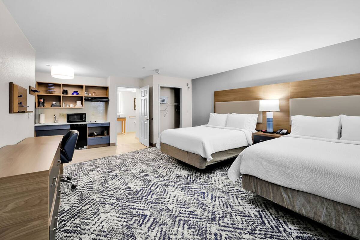Une chambre d’hôtel avec deux lits, un bureau, une chaise, un coin cuisine et une salle de bain.