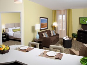 Ein Hotelzimmer mit einem Bett, einer Couch, einem Esstisch für zwei Personen und einem Fernseher.