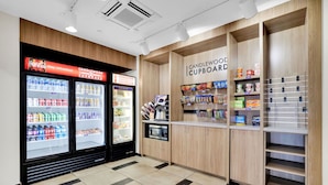 Una sección de una tienda con dispensadores refrigerados para bebidas, un microondas y estantes llenos de aperitivos y velas.
