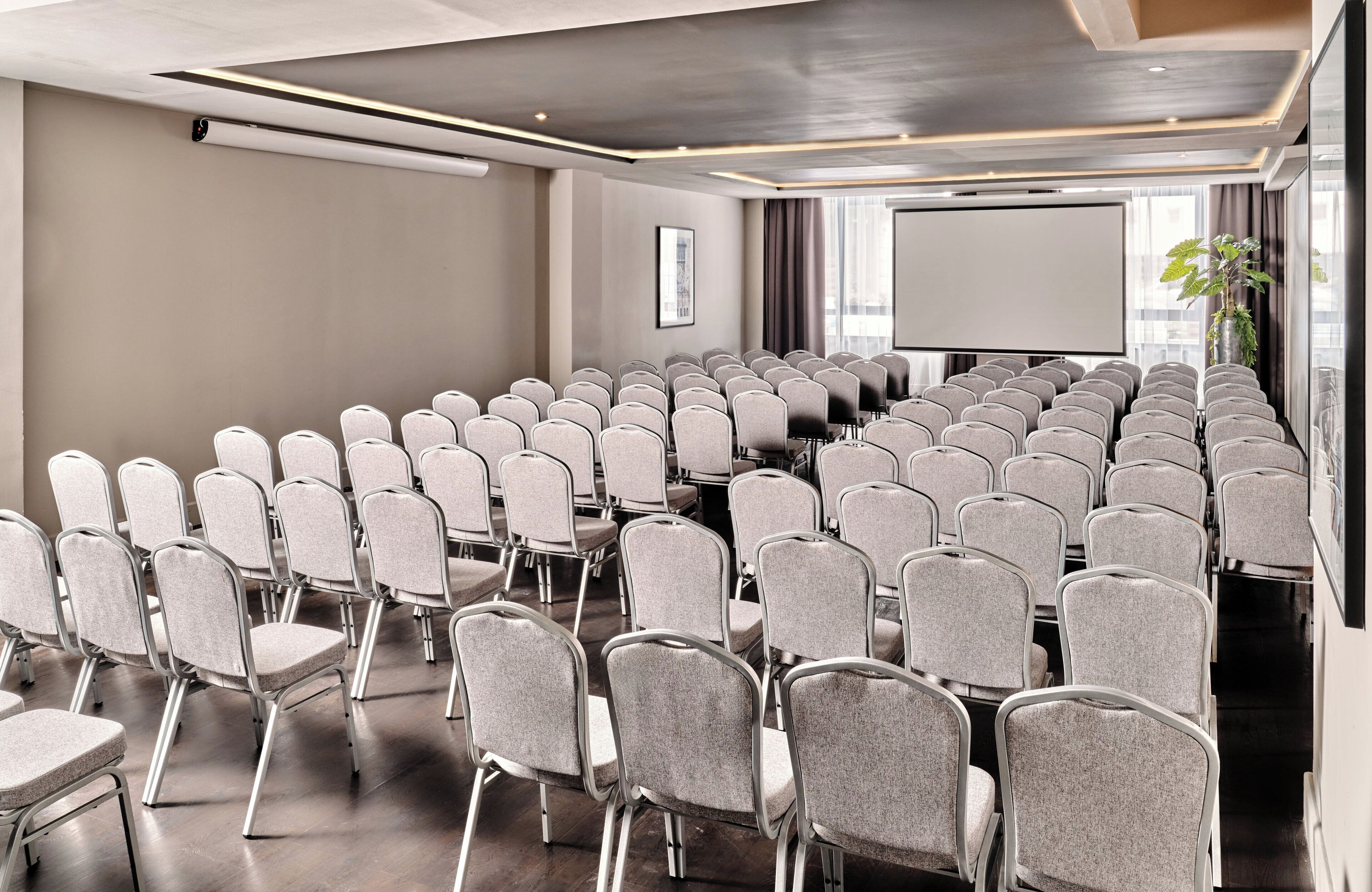 A conference room with rows of chairs, a projector screen, and a large window with curtains.