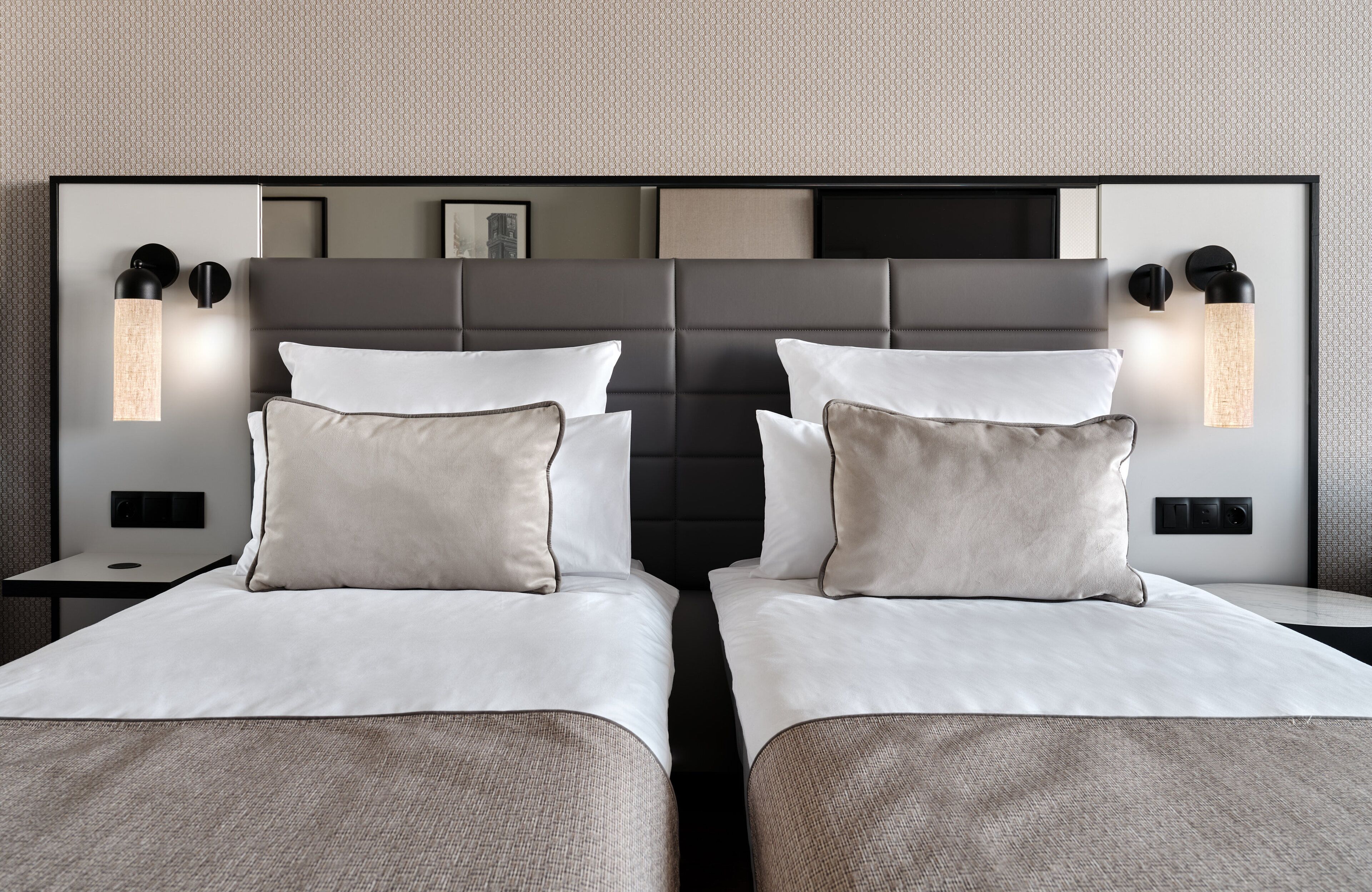 Habitación de hotel con dos camas, cada una con cabecero, lámparas de noche y una decoración en tonos neutros.