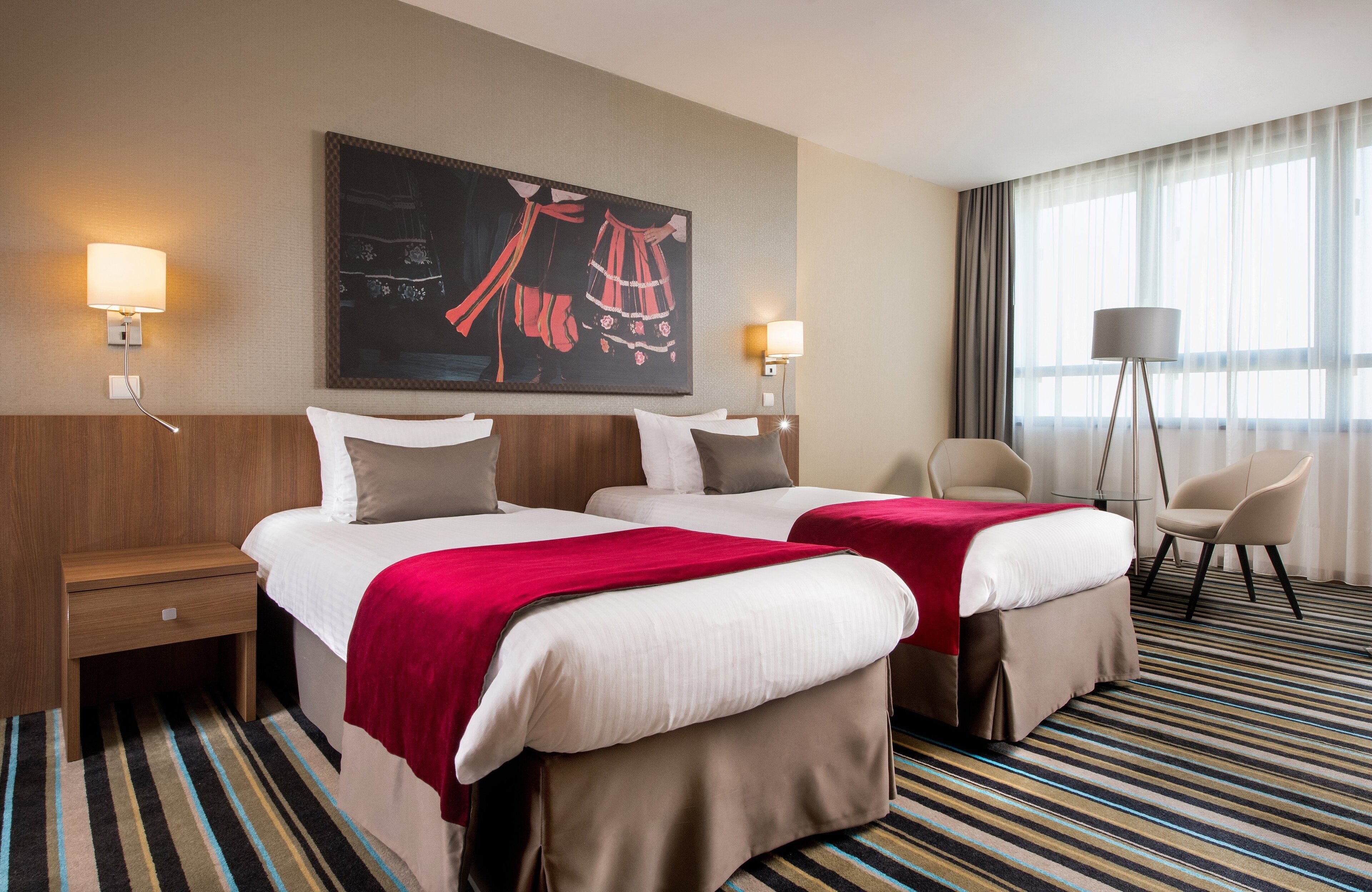 A hotel room with two beds, a desk, a chair, and a large painting on the wall.