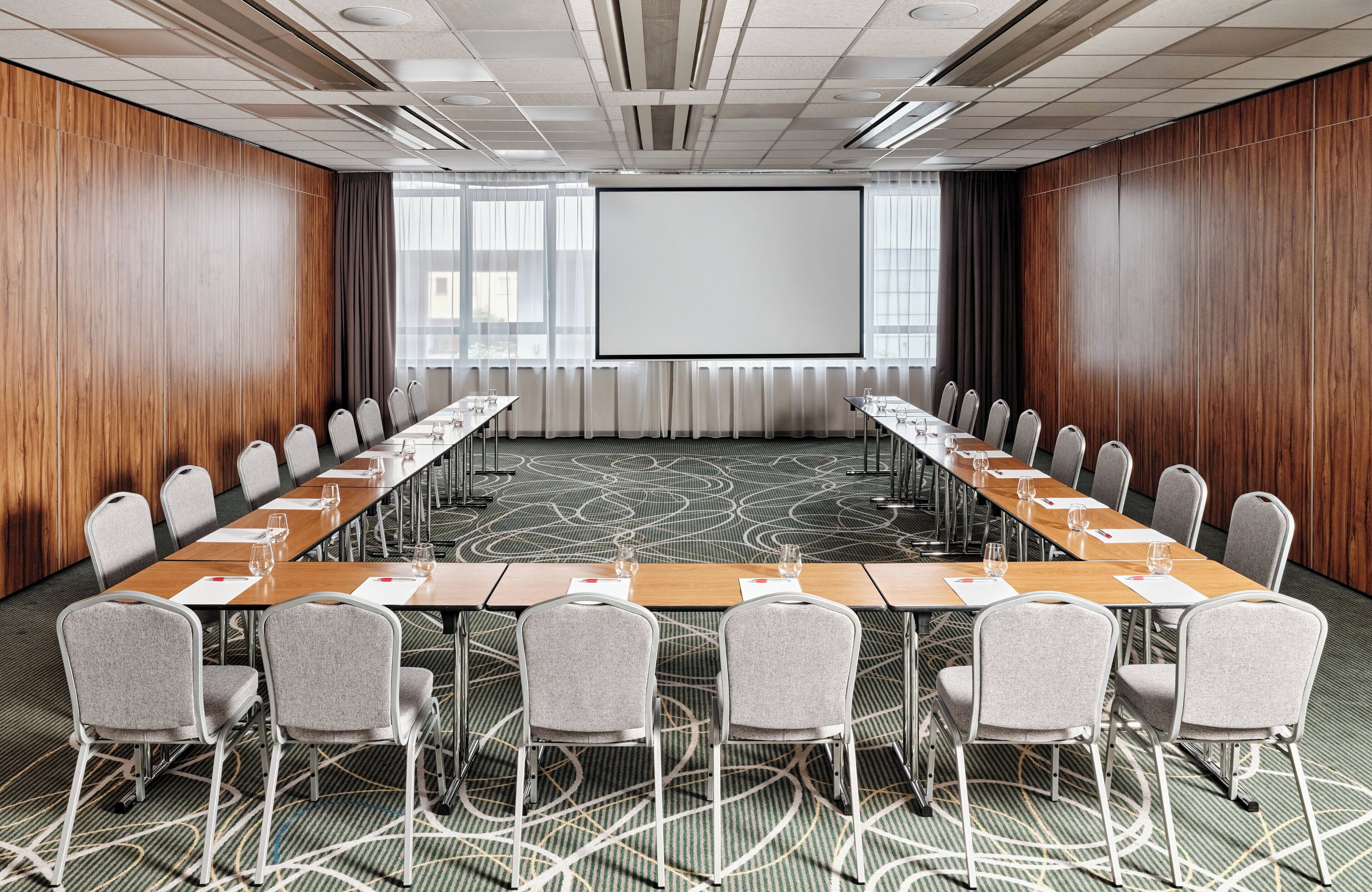A conference room with a long table, chairs, a projector screen, and a carpeted floor.