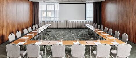A conference room with a long table, chairs, a projector screen, and a carpeted floor.