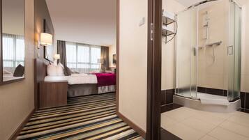 A hotel room with a bed, bedside table, lamp, and a shower area with a glass door.
