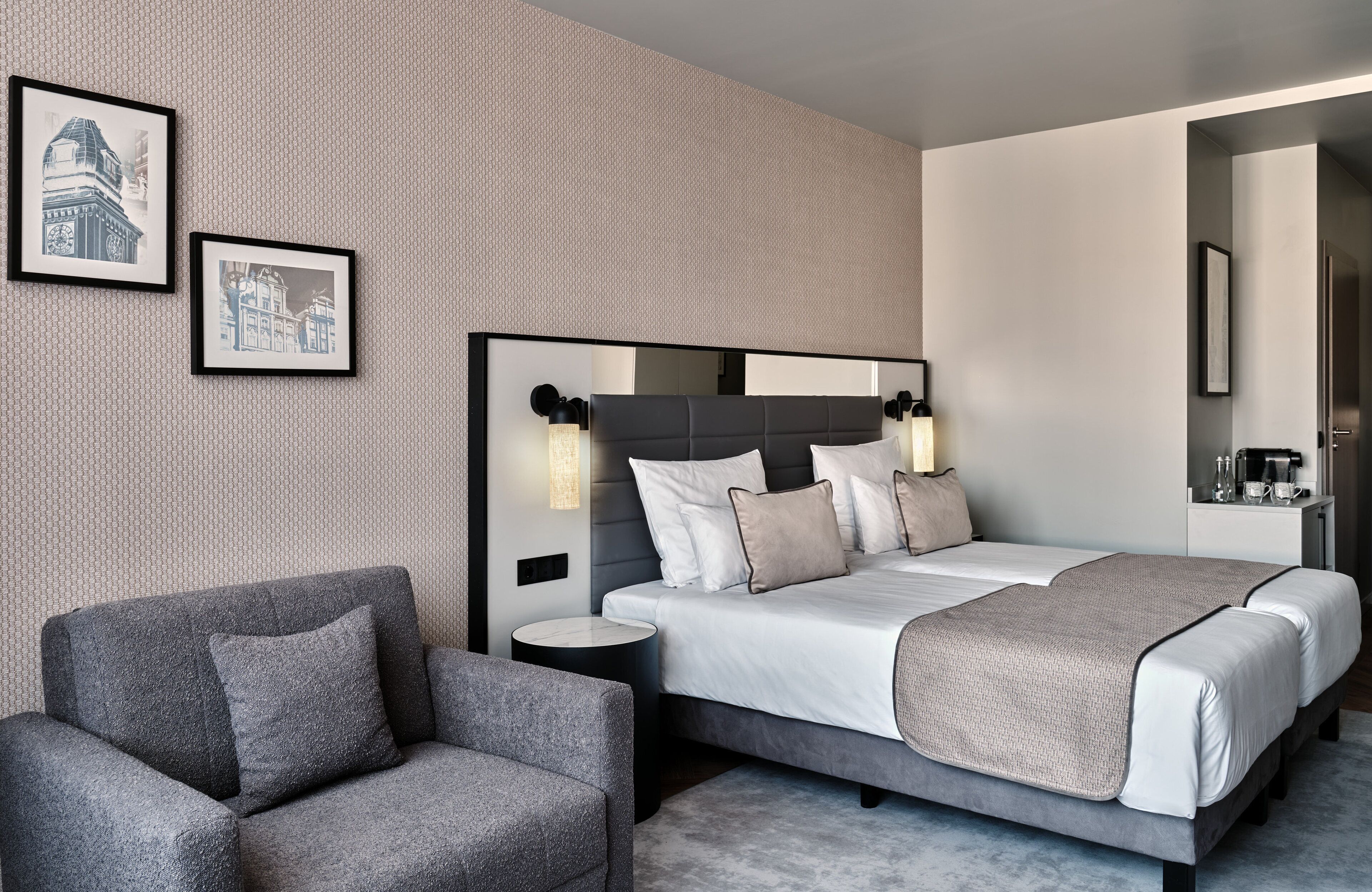 A modern hotel room with a large bed, a side table, a chair, and two framed pictures on the wall.