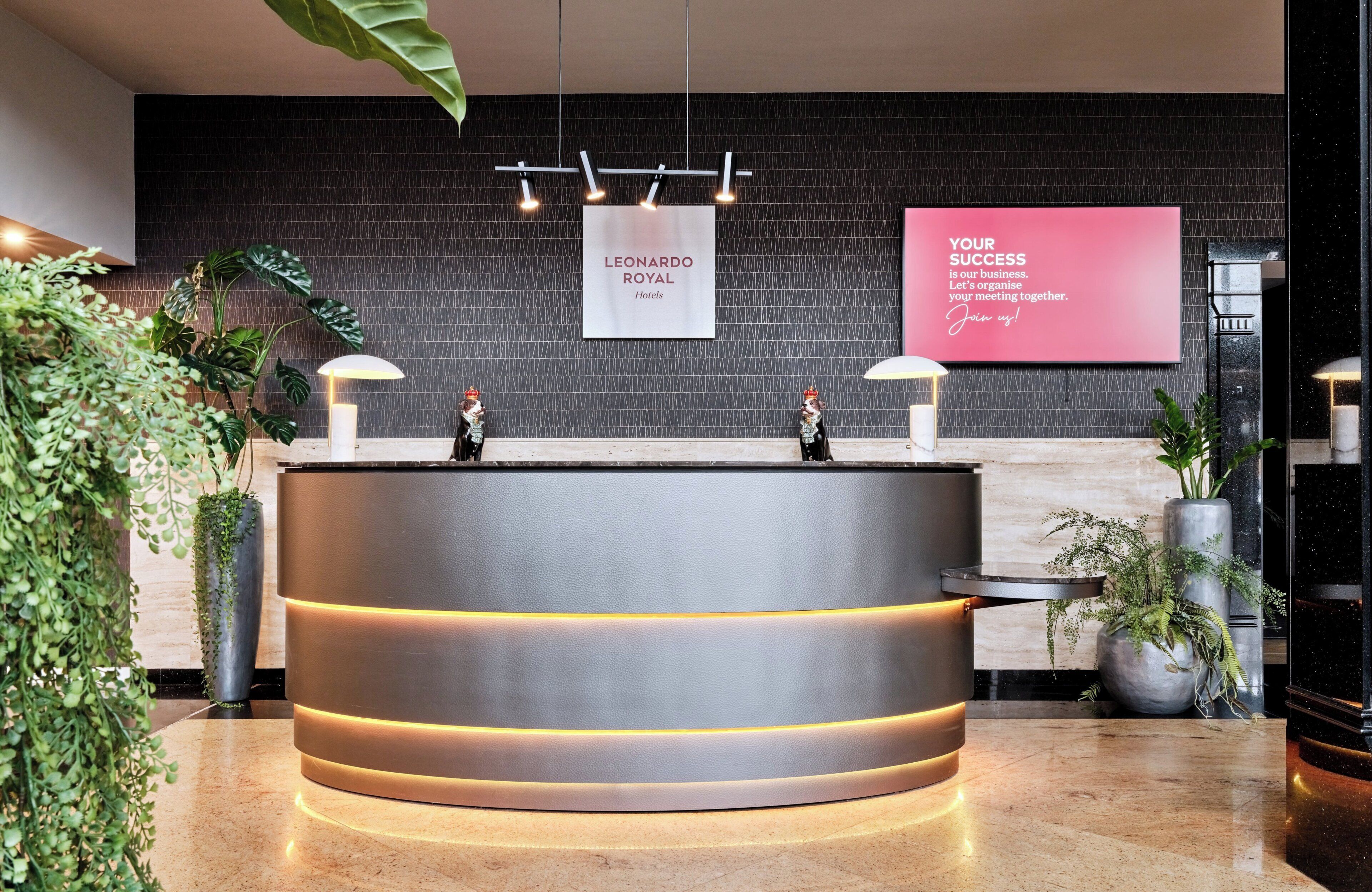 Una moderna recepción con encimera oscura, iluminación ambiental y un cartel que dice 'Leonardo Royal Hotels'.