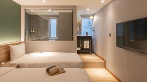 Une chambre d’hôtel avec deux lits, une télévision, une salle de bain avec douche et un petit coin salon agrémenté d’une plante.