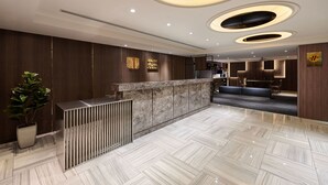 Un hall d’hôtel moderne avec un comptoir d’accueil, un espace salon et une grande plante en pot.