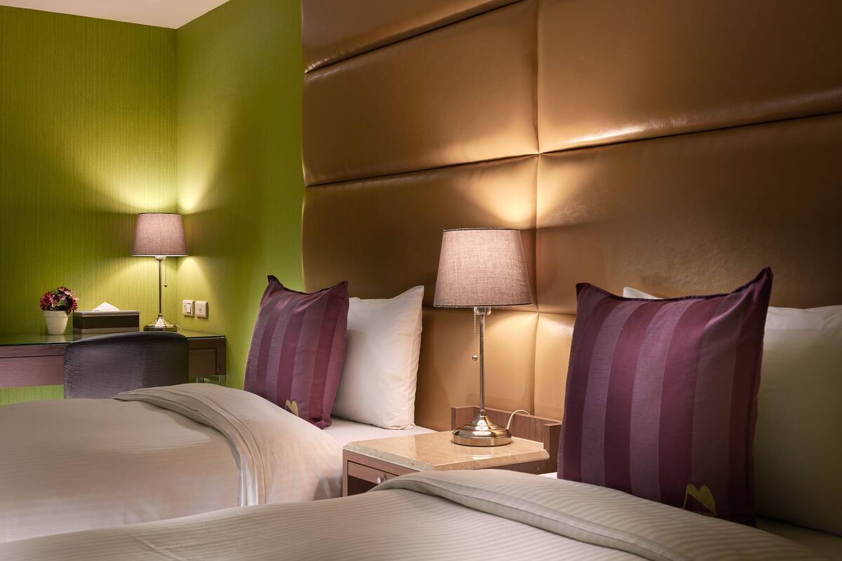 Ein Hotelzimmer mit zwei Betten, einem Kopfteil, Nachttischen mit Lampen und einem Beistelltisch mit Lampe.