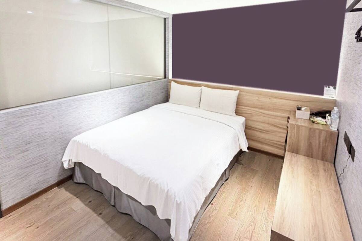 Ein modernes Schlafzimmer mit einem großen Bett, einem Holzkopfteil, einem Nachttisch und einer Trennwand aus Glas.