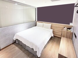 Een moderne slaapkamer met een groot bed, een houten hoofdbord, een nachtkastje en een glazen scheidingswand.