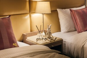 Een hotelkamer met een bed, een nachtkastje met een lamp, een decoratief konijn en een paar brillen.