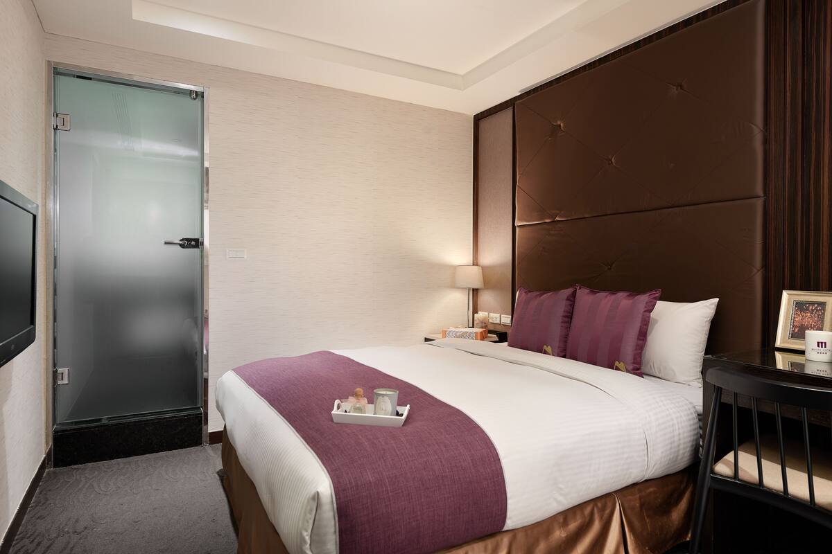 Ein Hotelzimmer mit Bett, Nachttisch, Lampe und Fernseher.
