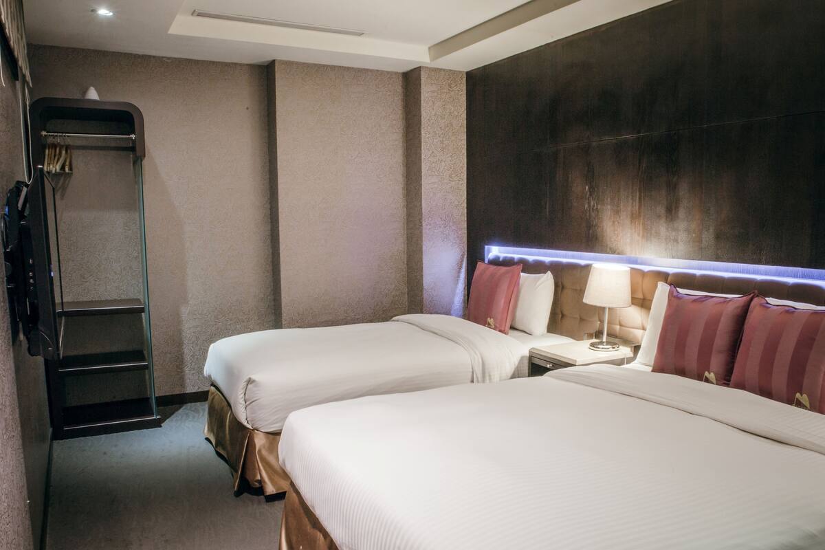 Ein Hotelzimmer mit zwei Betten, einem Nachttisch mit Lampe, einem Kleiderschrank und einem großen Fenster mit Blick.