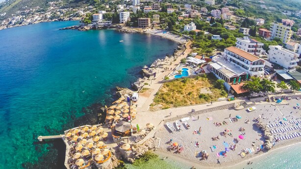An aerial view of a coastal town with clear blue waters, a sandy beach, and buildings along the shore. - David Dobre Vode (Bar)