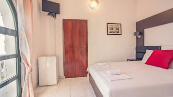 Quarto de hotel com cama, televisão presa à parede, uma porta e um eletrodoméstico branco pequeno.