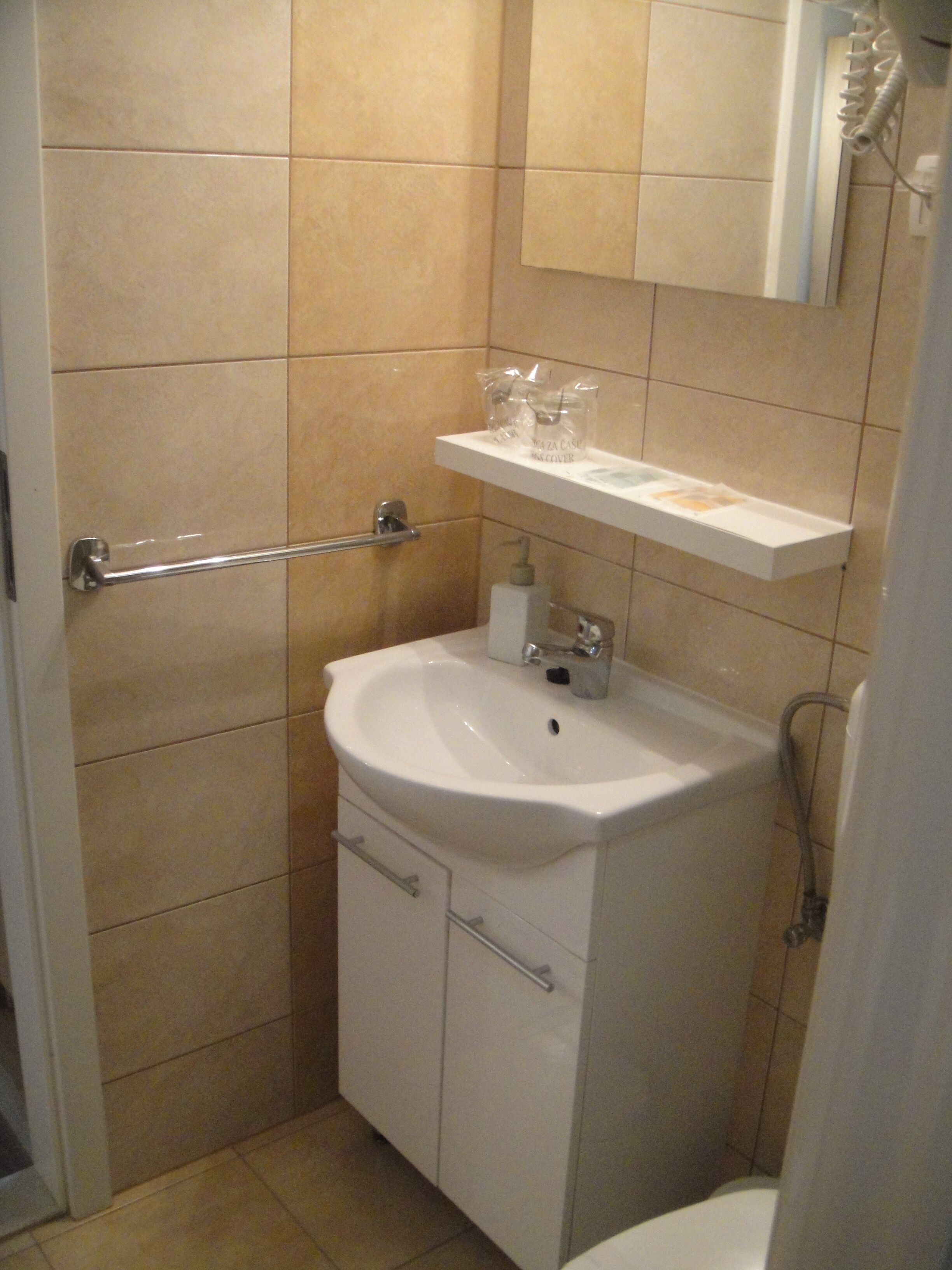 Un baño con un lavamanos blanco, un espejo encima y un perchero para toallas.
