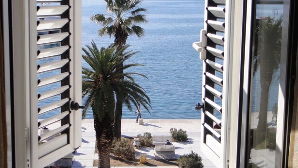 A window with open shutters, offering a view of a palm tree and the sea. - B&B Central Palace Heritage (Split)