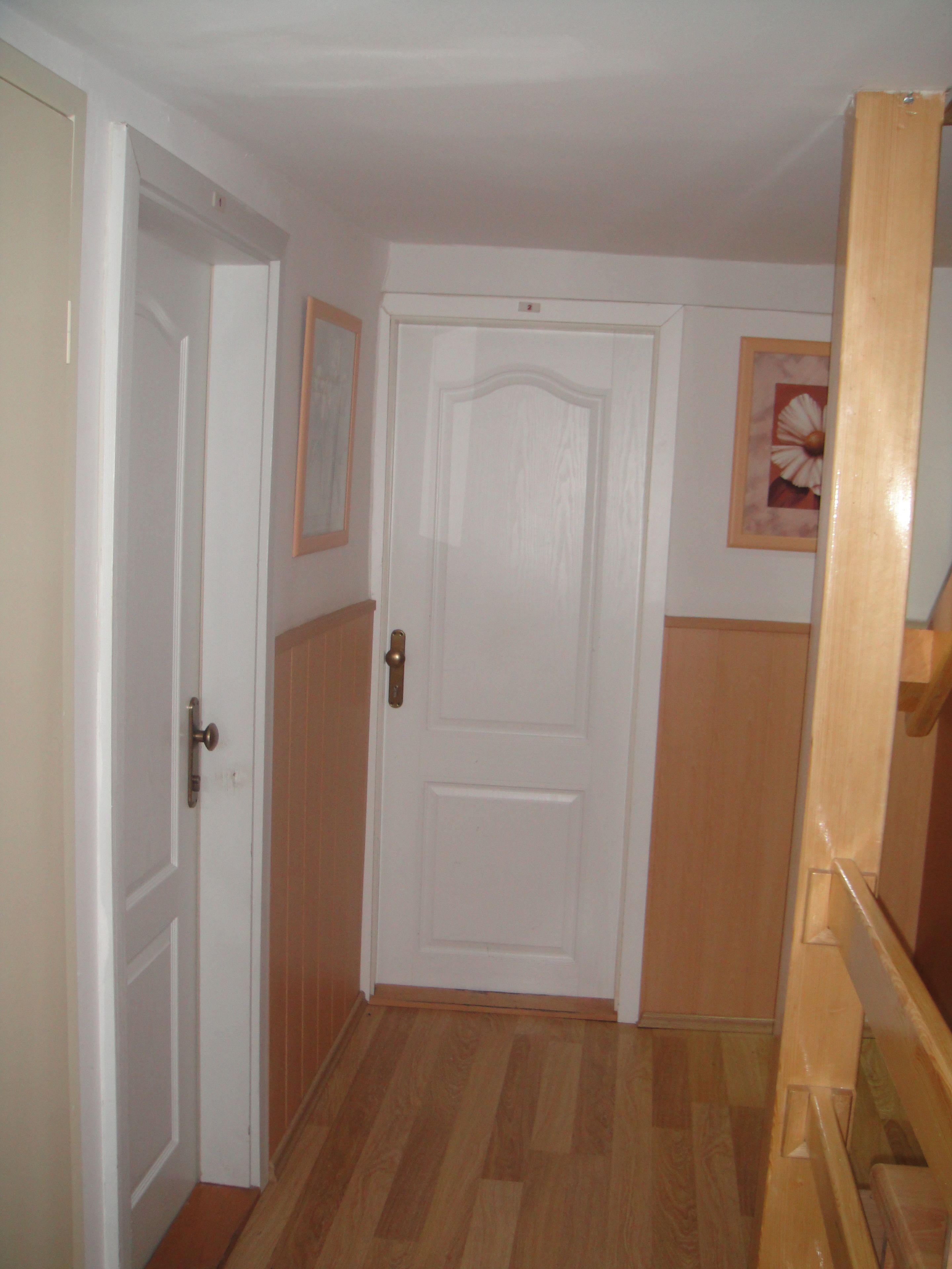 A hallway with a white door, wooden floor, and a wooden staircase.