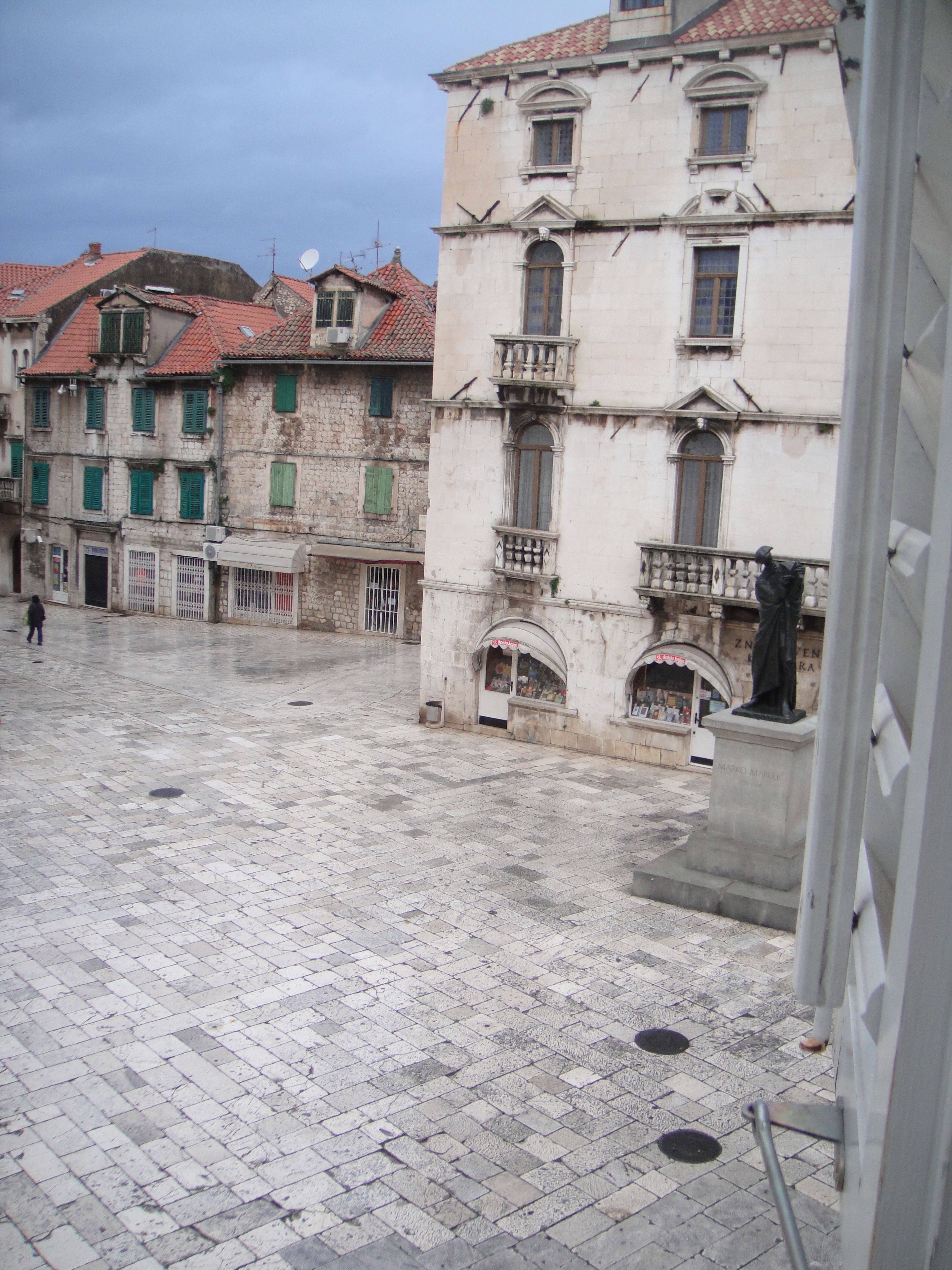 Un cortile con pavimento in piastrelle, una statua ed edifici storici con balconi e tetti in tegole rosse.
