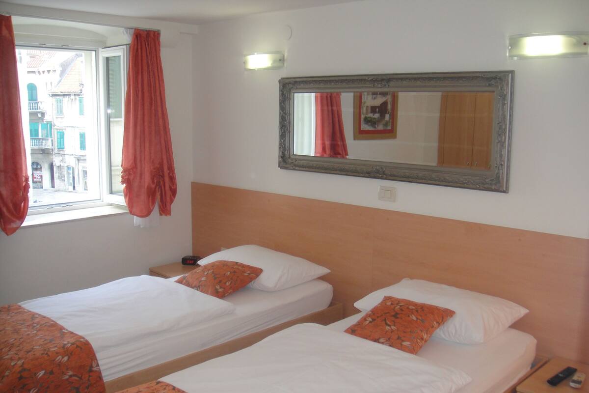 Ein Hotelzimmer mit zwei Betten, einem Nachttisch, einem Spiegel und einem Fenster mit Vorhängen.