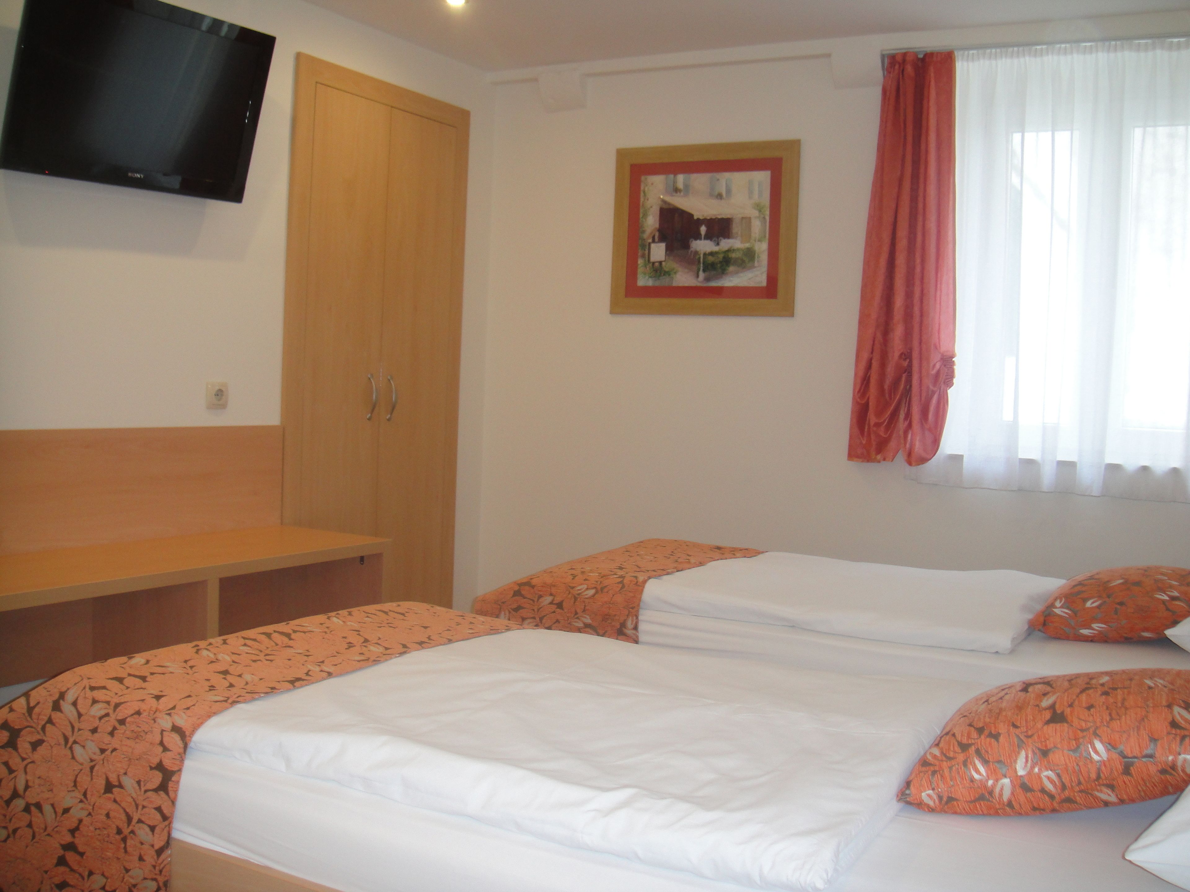 A hotel room with two beds, a wooden wardrobe, a flat-screen TV, and a painting on the wall.